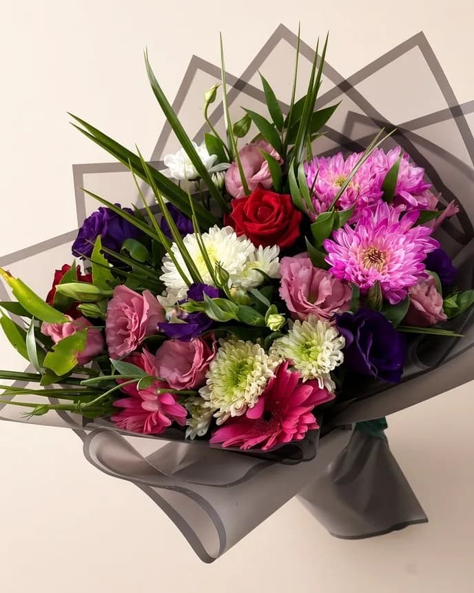 Gri şeffaf ambalajda lisianthus, kırmızı gül ve fuşya gerberalardan buket