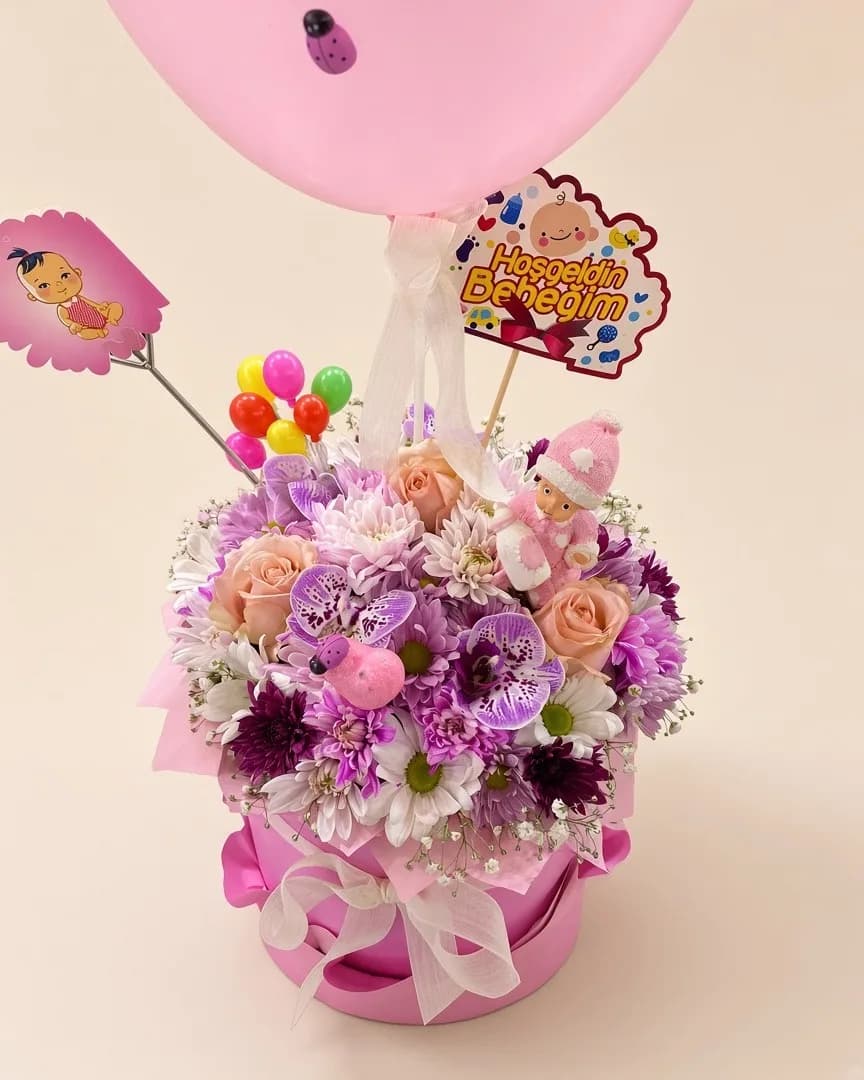 Pembe kutuda orkide, gül ve kasımpatılar; pembe balon ve hoş geldin bebeğim süsü