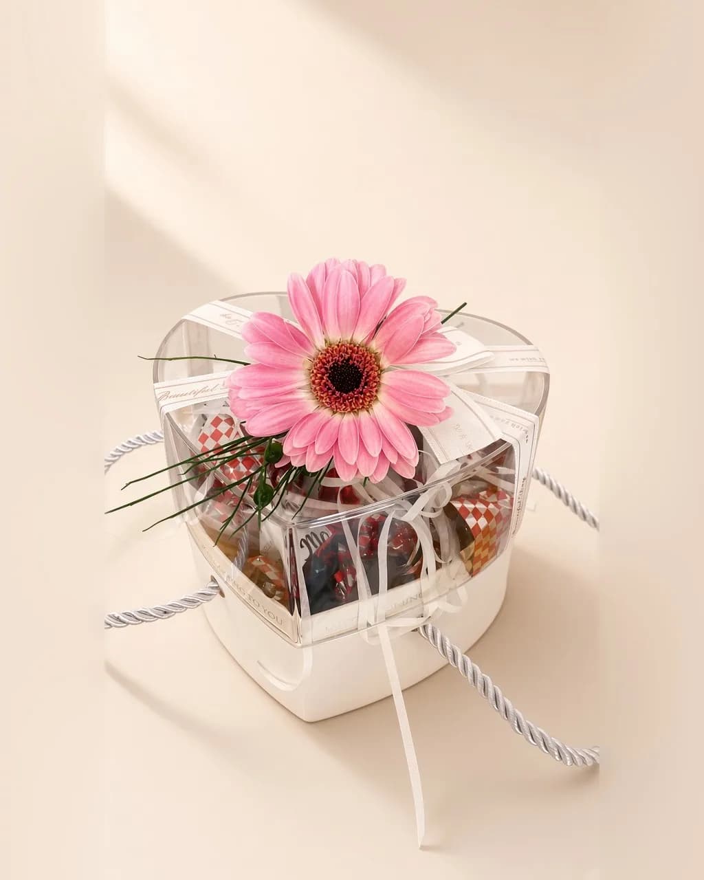 Şeffaf kalp kutuda çikolatalar ve kapağında pembe gerbera