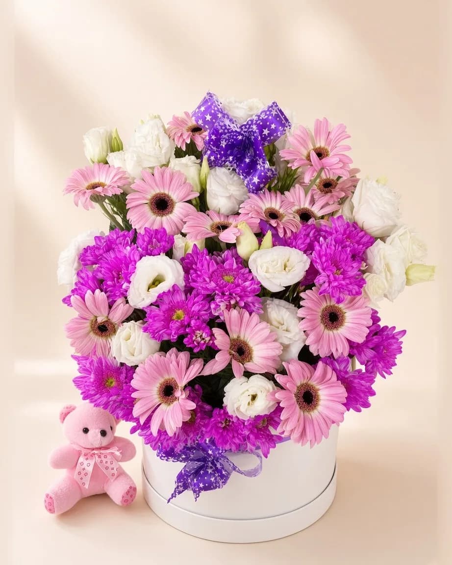 Beyaz kutuda pembe gerbera, mor krizantem ve beyaz lisianthus aranjmanı, yanında pembe peluş ayıcık