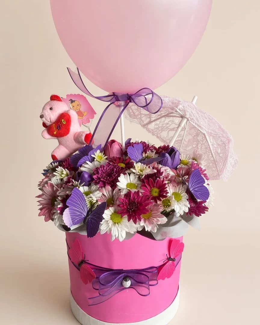 Pembe kutuda mor ve beyaz kasımpatılar, kelebek süsleri, peluş ayıcık ve pembe balon