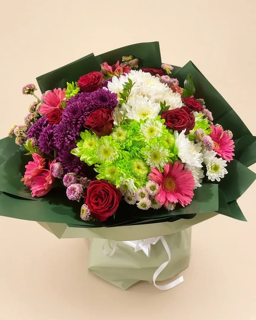 Yeşil ambalajda kırmızı gül, pembe gerbera ve renkli kasımpatılardan buket